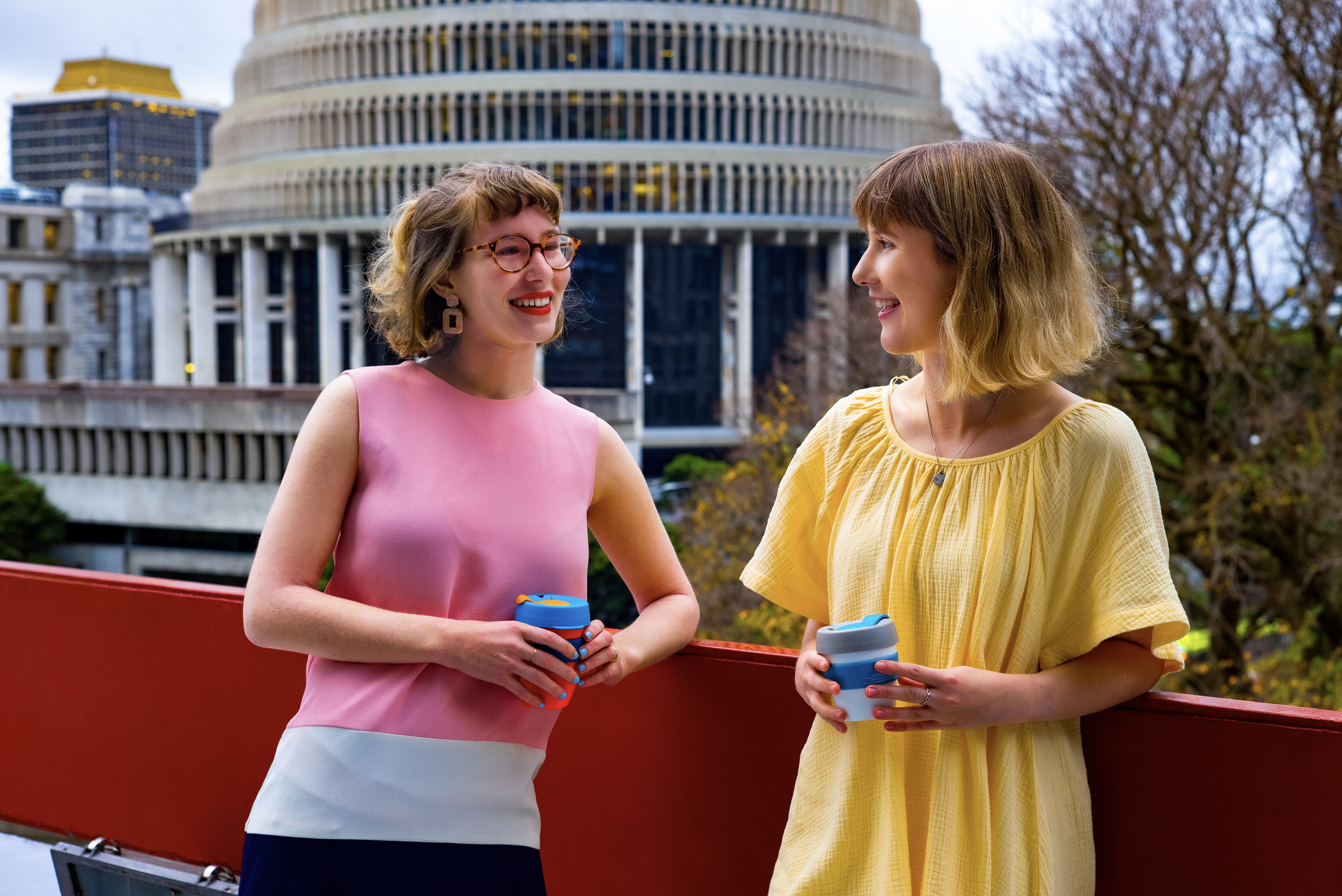 Two women standing on a balcony with the Beehive in the background