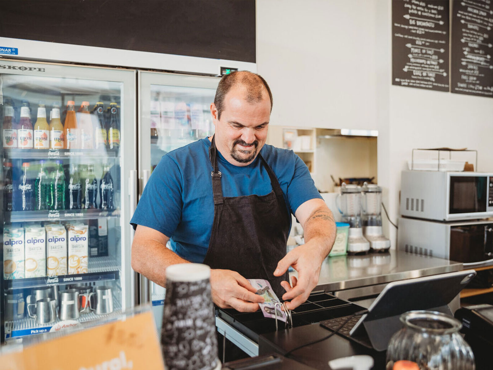 Man behind a cash register in a cafe with a $50 note