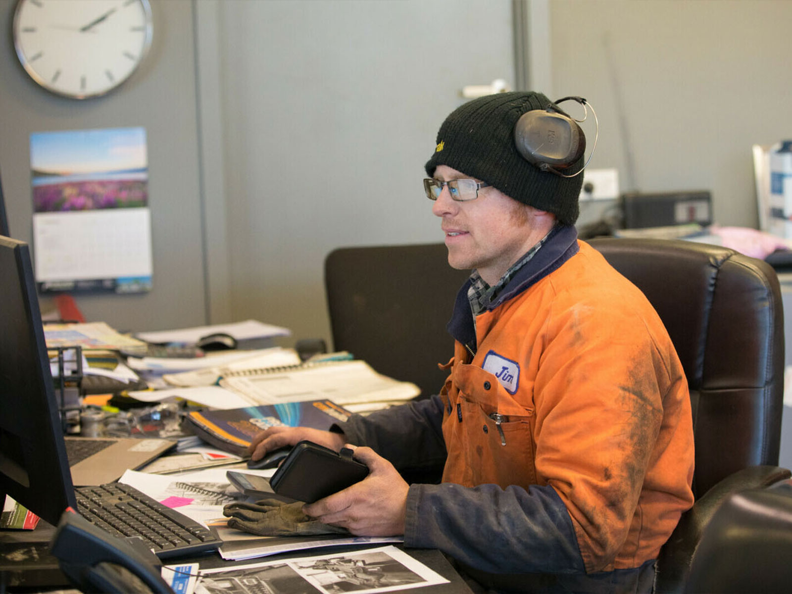 Man in orange jumpsuit and black beanie sitting at a desk looking at his computer