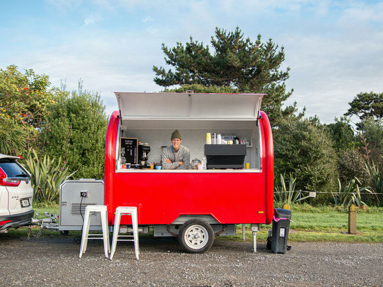 Man in a green beanie operating a red coffee cart