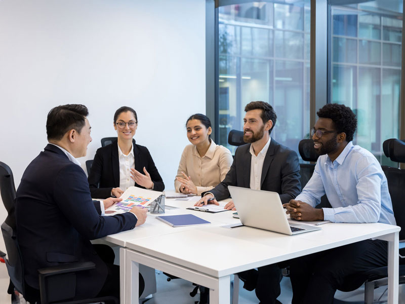 A group of professional office workers sitting around a table attending a meeting. 