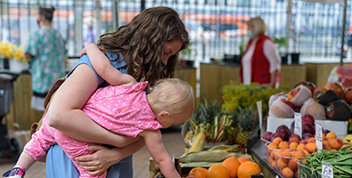 Woman buying vegetables with baby girl on farmers food market